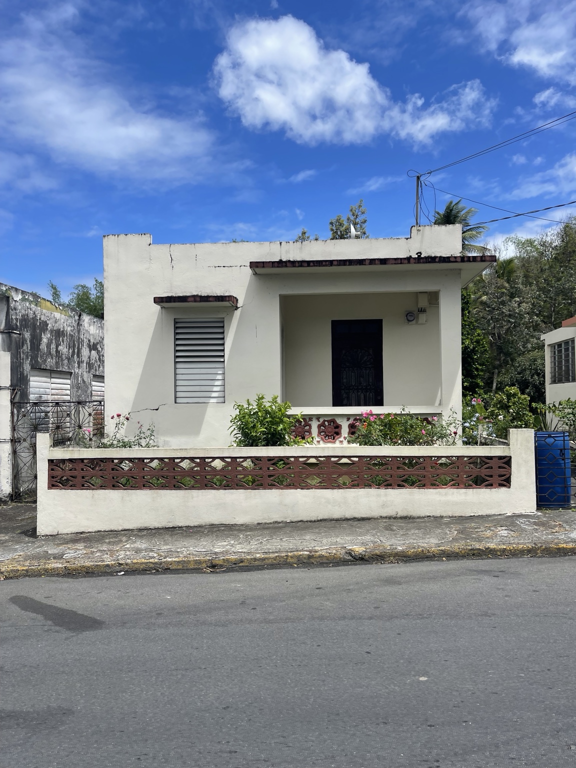 Vivienda de una unidad en concreto, con techo plano, balcón frontal y muro de bloques ornamentales.