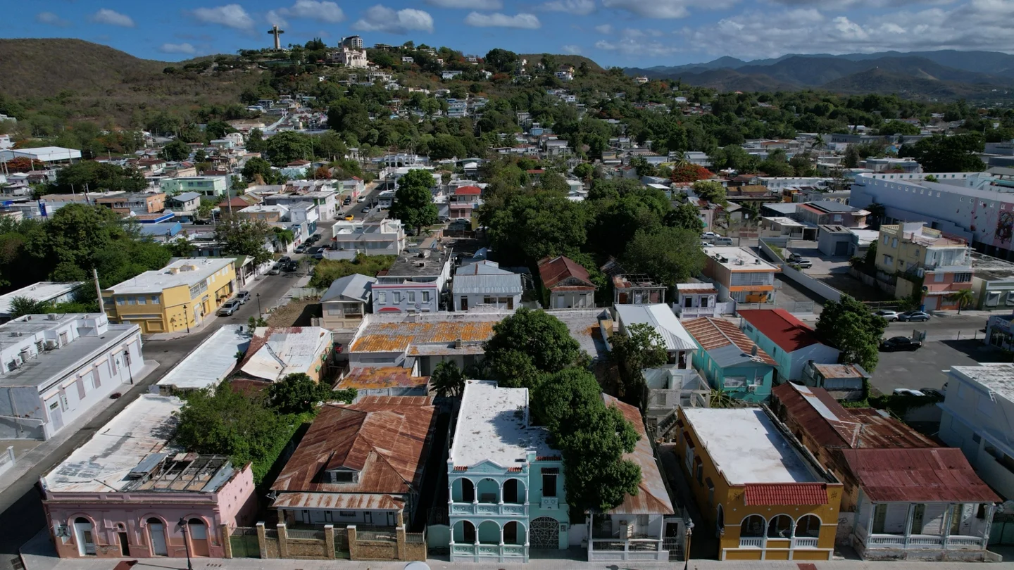Vista aérea de Ponce: fachadas tradicionales y viviendas del casco urbano en primer plano, con las montañas al fondo.